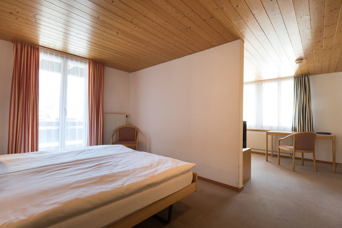 A bedroom with a wooden ceiling, a bed, a desk, and a chair.