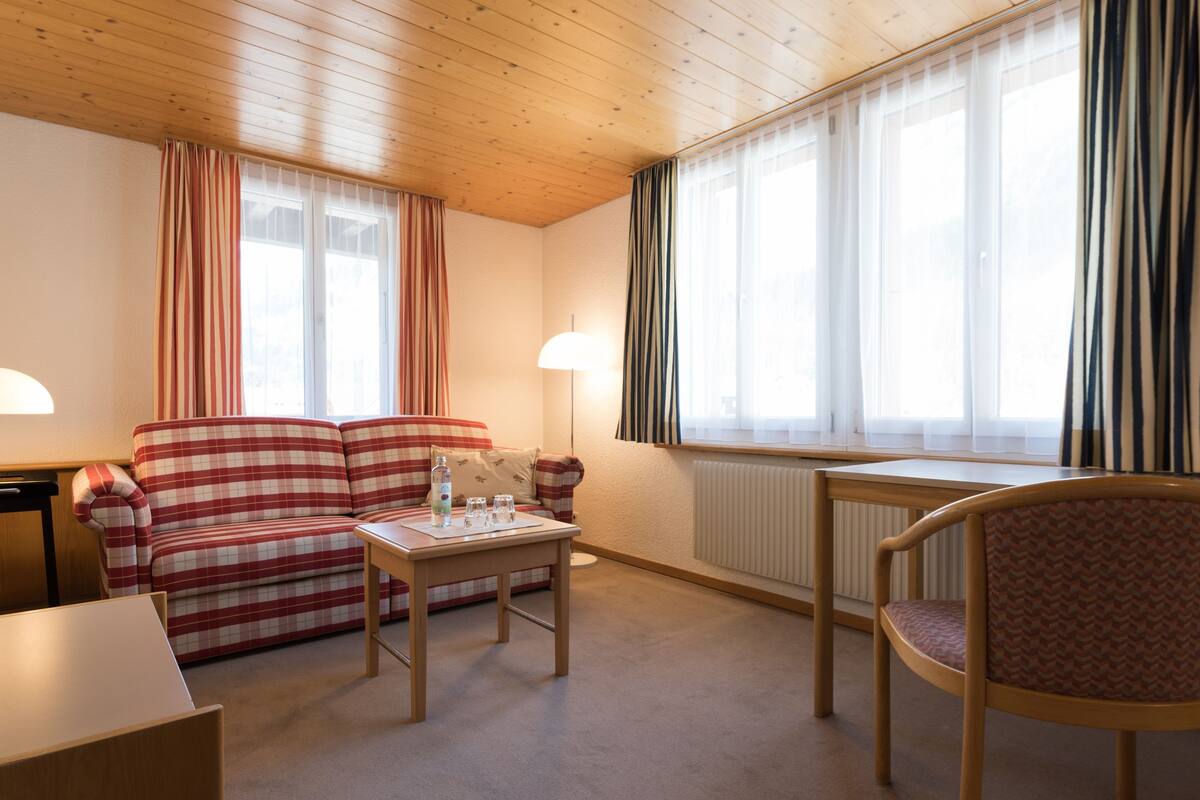 A cozy living room with a plaid sofa, a small table with glasses, a chair, and a radiator.