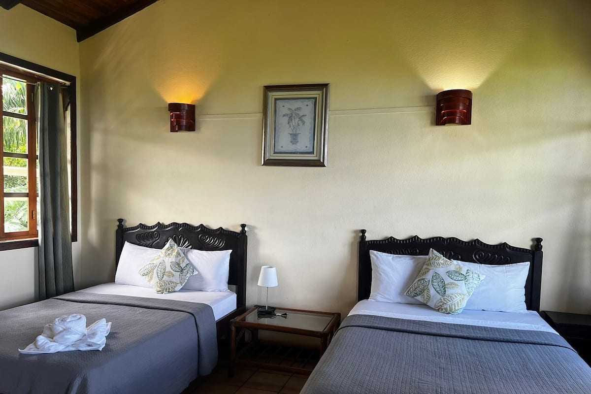 A hotel room with two beds, a nightstand, a framed picture on the wall, and a window with curtains.