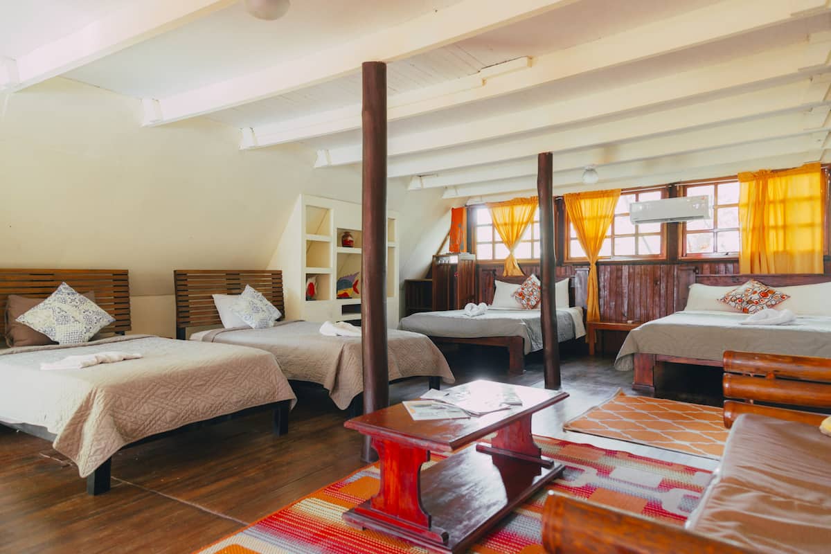 A hotel room with three beds, wooden furniture, and a large window with curtains.