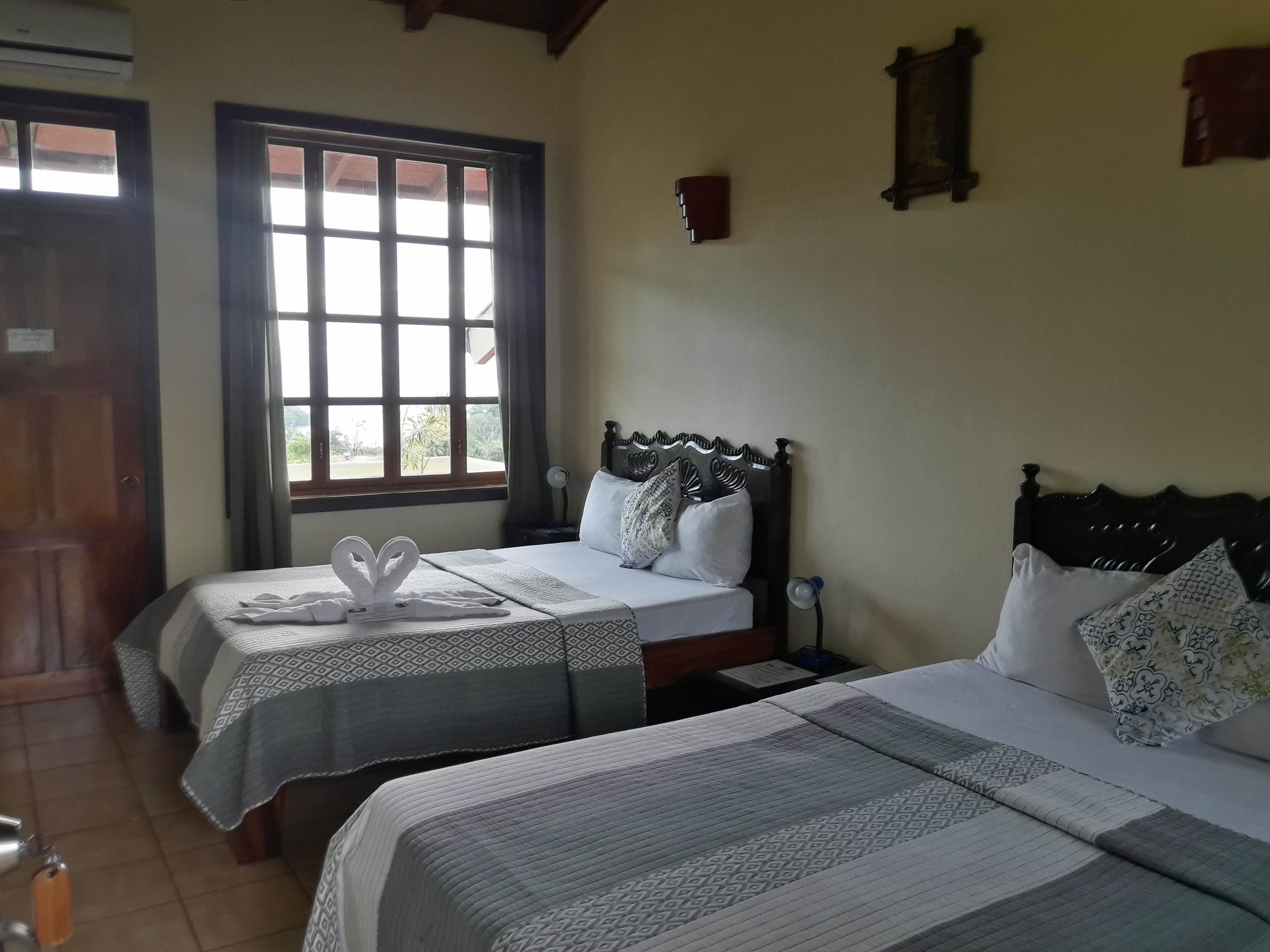 Una habitación de hotel con dos camas, una ventana con cortinas, una mesita de noche y un reloj en la pared.