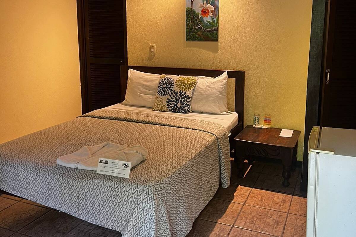 A bedroom with a bed, a nightstand, a painting, and a ceiling fan.
