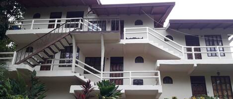 A multi-story building with balconies, staircases, and a garden area with various plants.