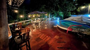 Un espace extérieur aménagé avec une terrasse, une piscine, des coins salon et des guirlandes lumineuses.