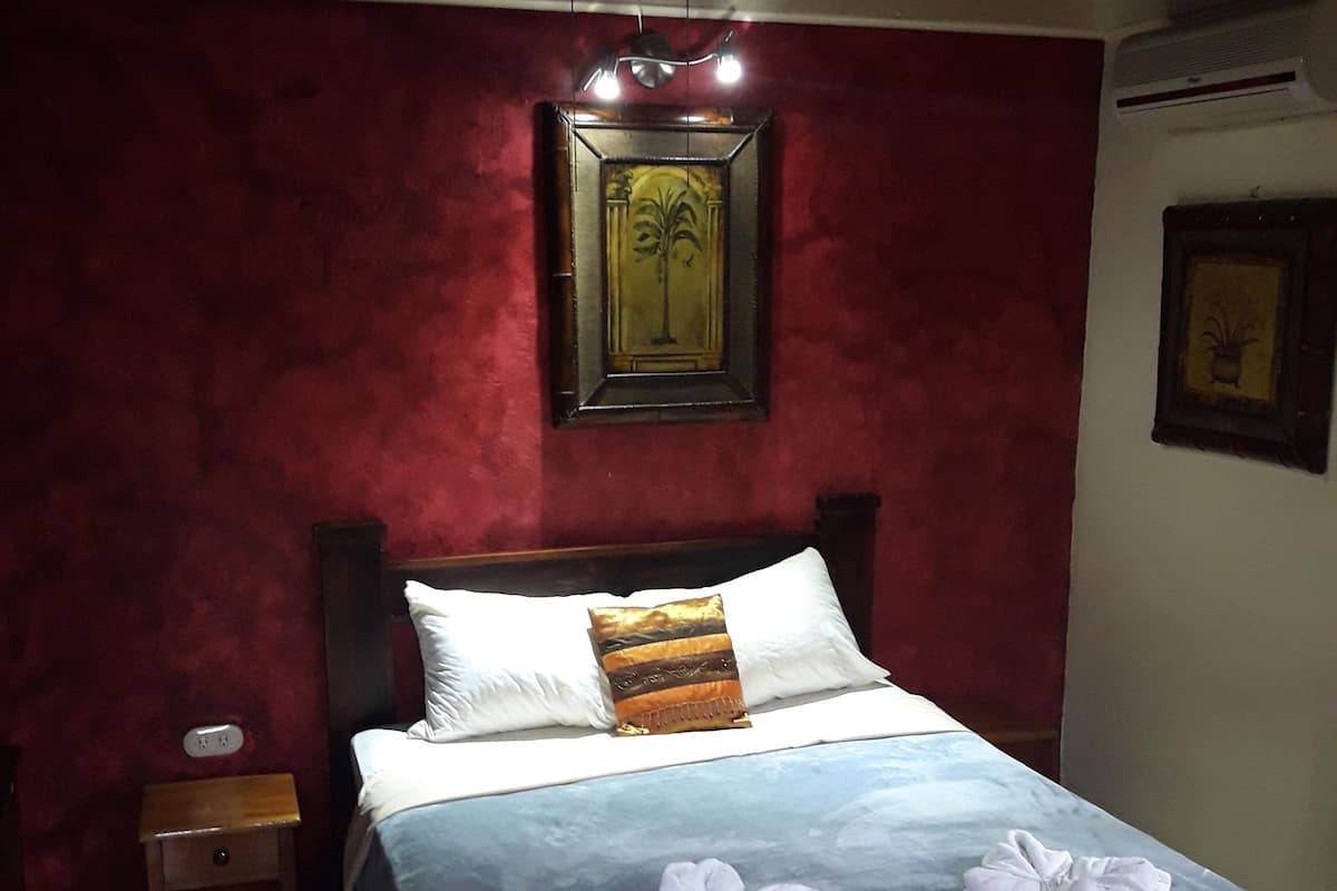 A bedroom with a bed, a nightstand, a ceiling fan, a wall-mounted air conditioner, and a framed picture.