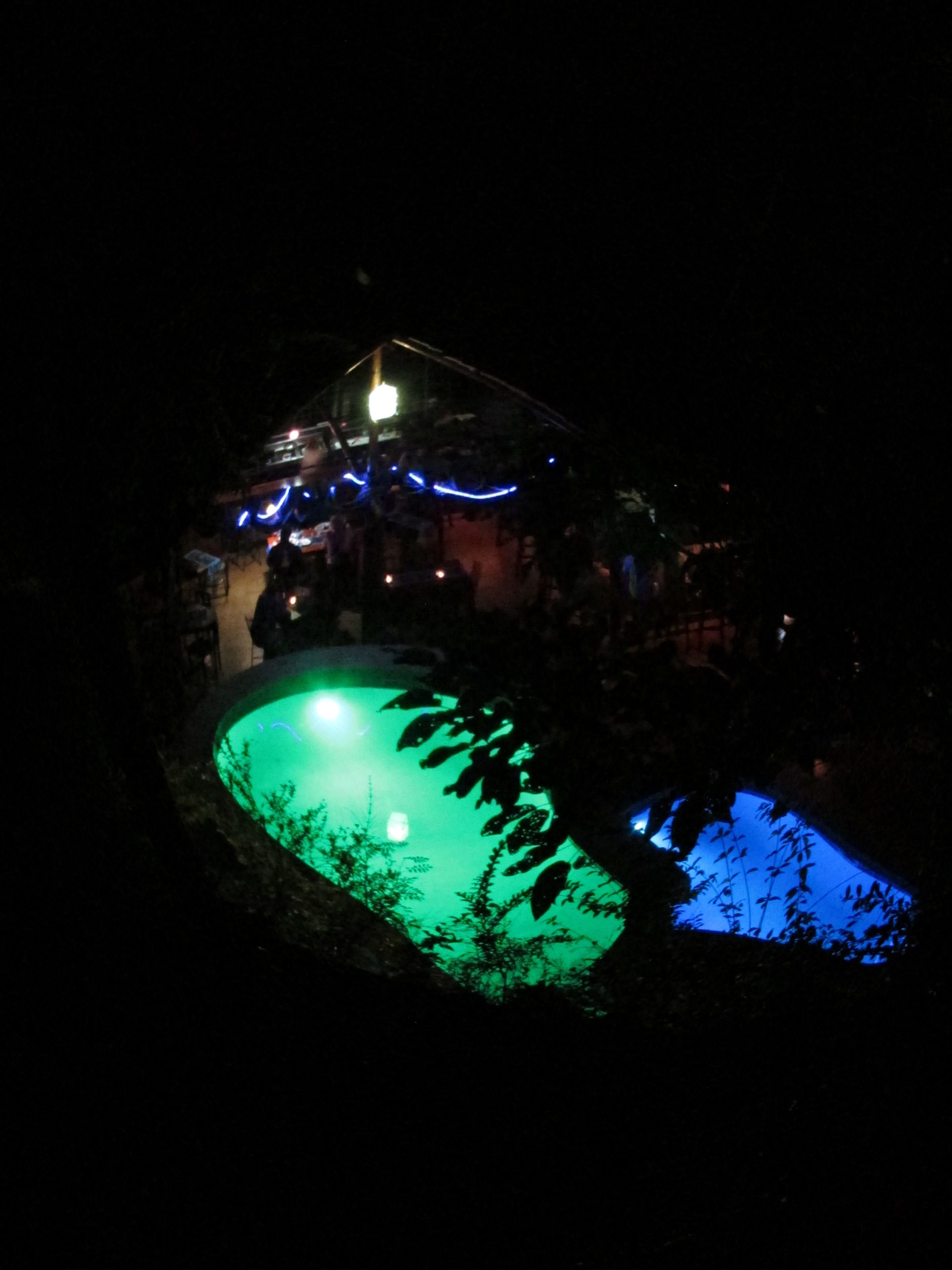 Vue nocturne d’un espace piscine avec une maison en arrière-plan.
