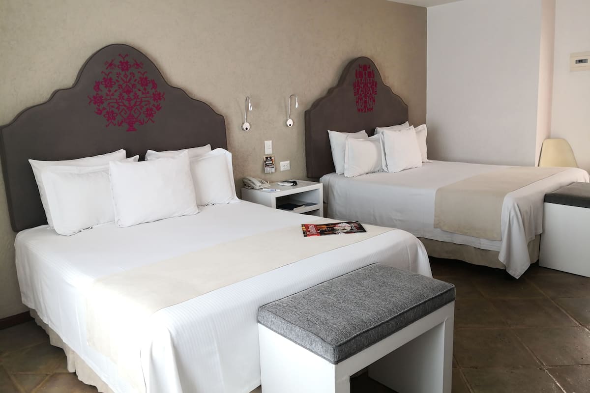 Una habitación de hotel con dos camas, un escritorio pequeño, una mesita de noche y un banco.