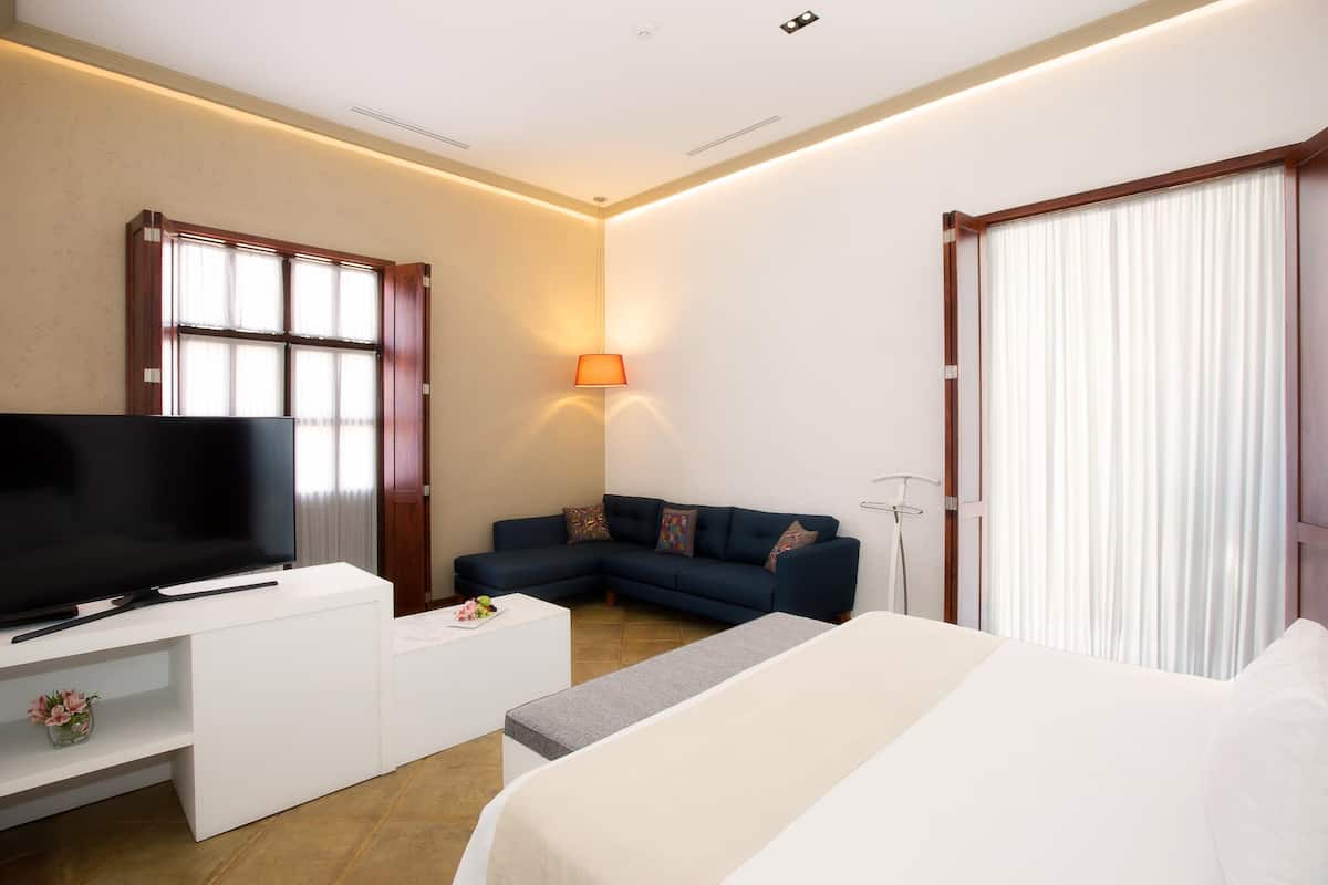 Una habitación de hotel moderna con televisión de pantalla plana, sofá, cama y ventana con cortinas.