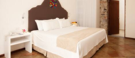 Una cama bien hecha con cabecera de madera, una mesita de noche con lámpara y un frutero pequeño.