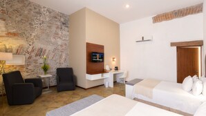 Habitació d'hotel amb paret de pedra, un televisor fixat a la paret, escriptori amb cadira, llit i una taula petita amb una làmpada.