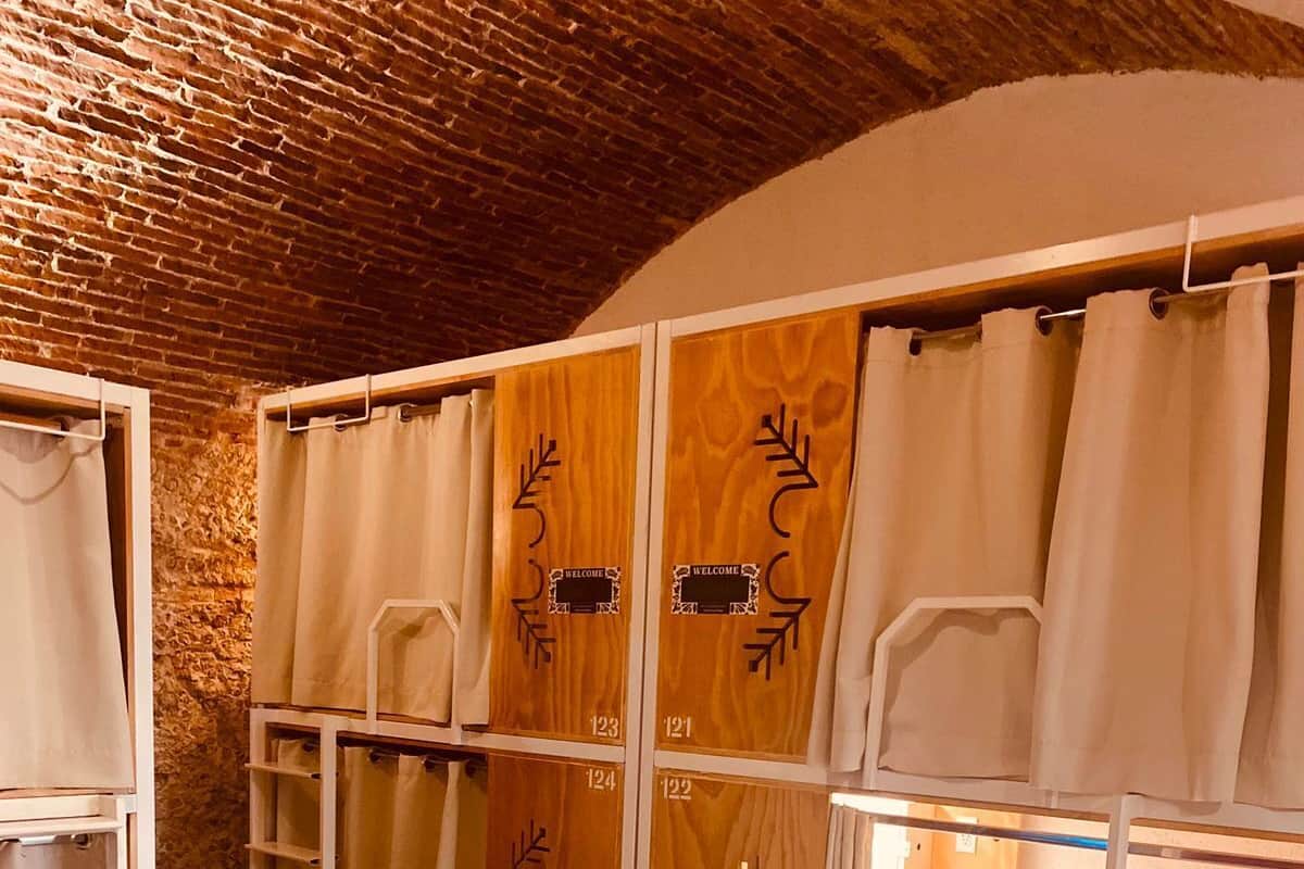 Una habitación con literas, paneles de madera con letreros de 'WELCOME' y una pared de piedra.