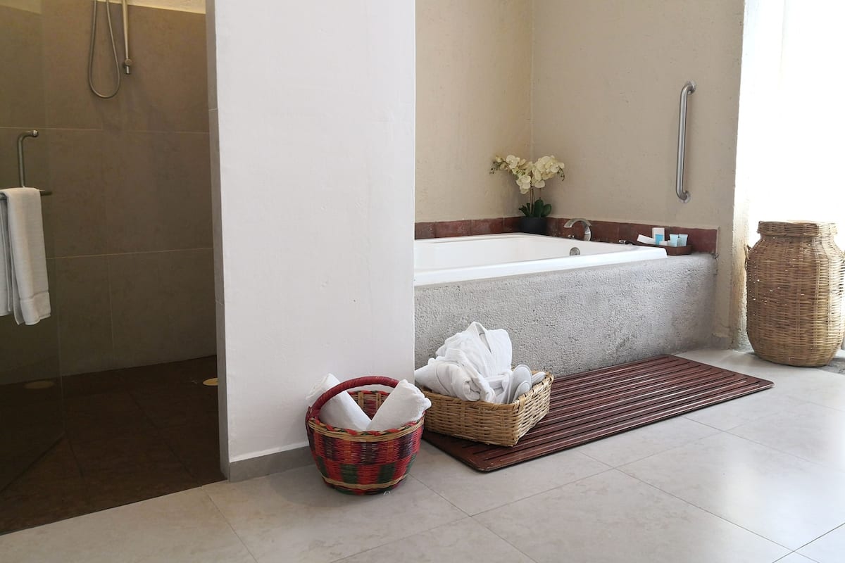 Un baño con ducha, bañera, lavamanos y una cesta de mimbre con toallas.