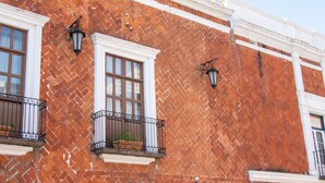Un edifici de maó amb adorns blancs, dues finestres amb baranes negres i dos fanals fixats a la paret.