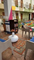 Een gezellig buiten zitgedeelte met een witte poef, een vloerkleed met patroon en een boekenkast met boeken en bloemen.