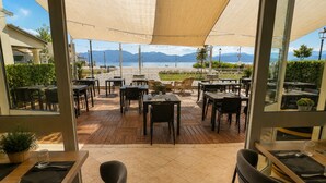 An outdoor dining area with tables and chairs, a view of the sea, and mountains in the background. - Hotel Butterfly - We Suite (Viareggio)