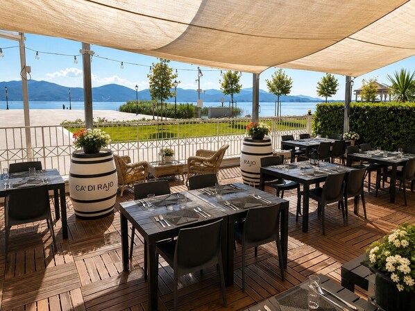 An outdoor dining area with tables and chairs, a view of the sea, and decorative plants.