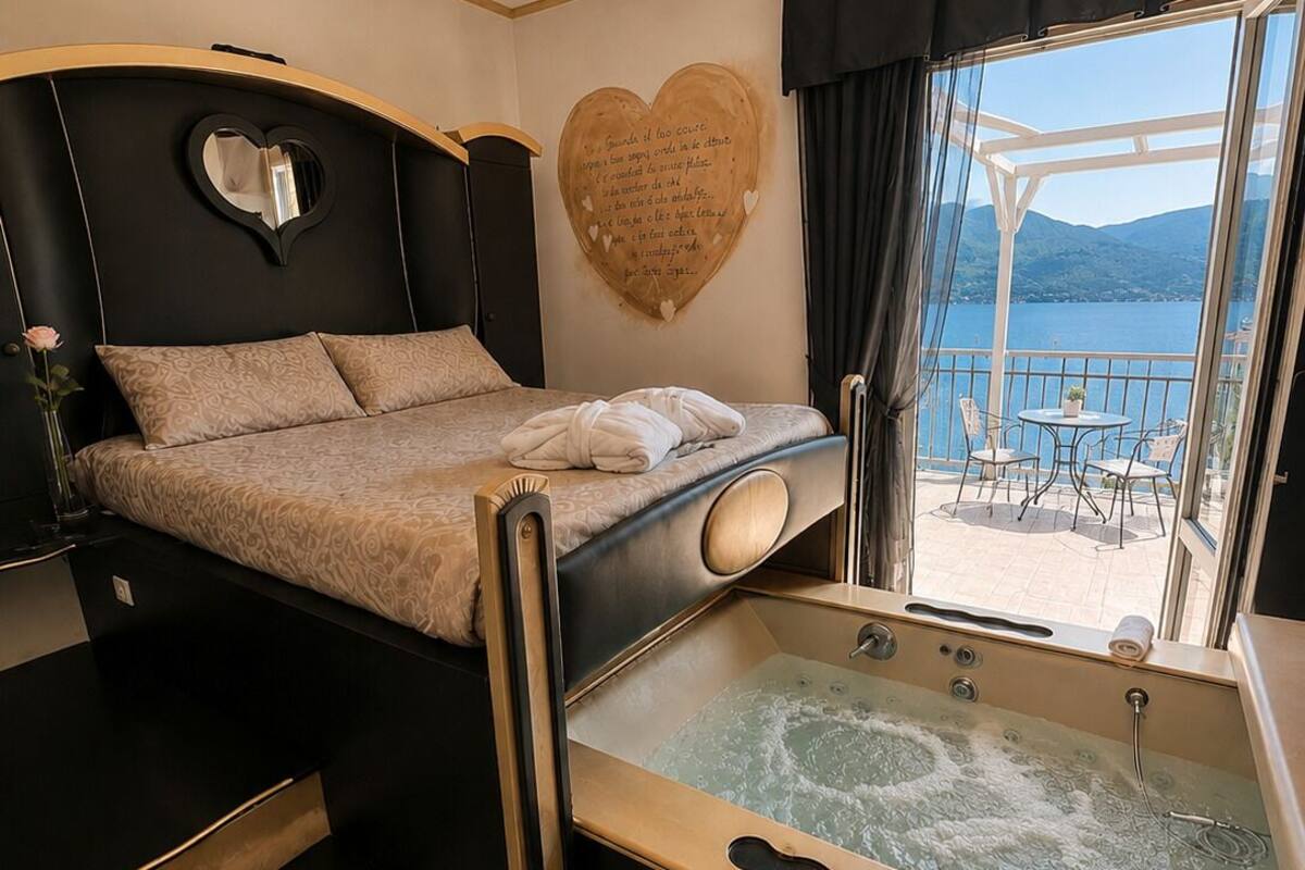 Una camera da letto con un letto, una decorazione a forma di cuore, una vasca da bagno e un balcone con vista sull'acqua.