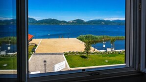 A view from a window overlooking a body of water with a distant mountain range, a paved area with benches, and a sign with text. - Hotel Butterfly - We Suite (Viareggio)