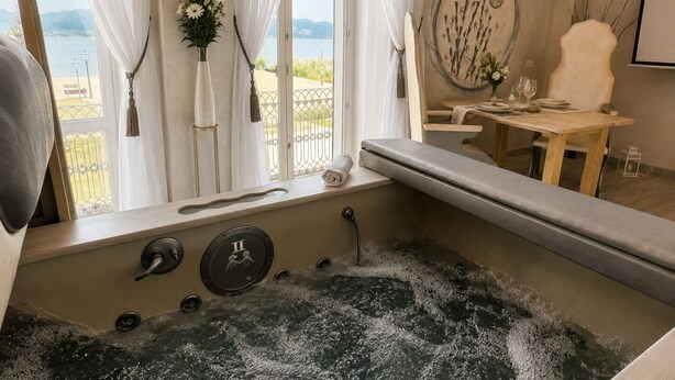 A bathroom with a bathtub, a window with curtains, a mirror, and a view of the outdoors. - Hotel Butterfly - We Suite (Viareggio)