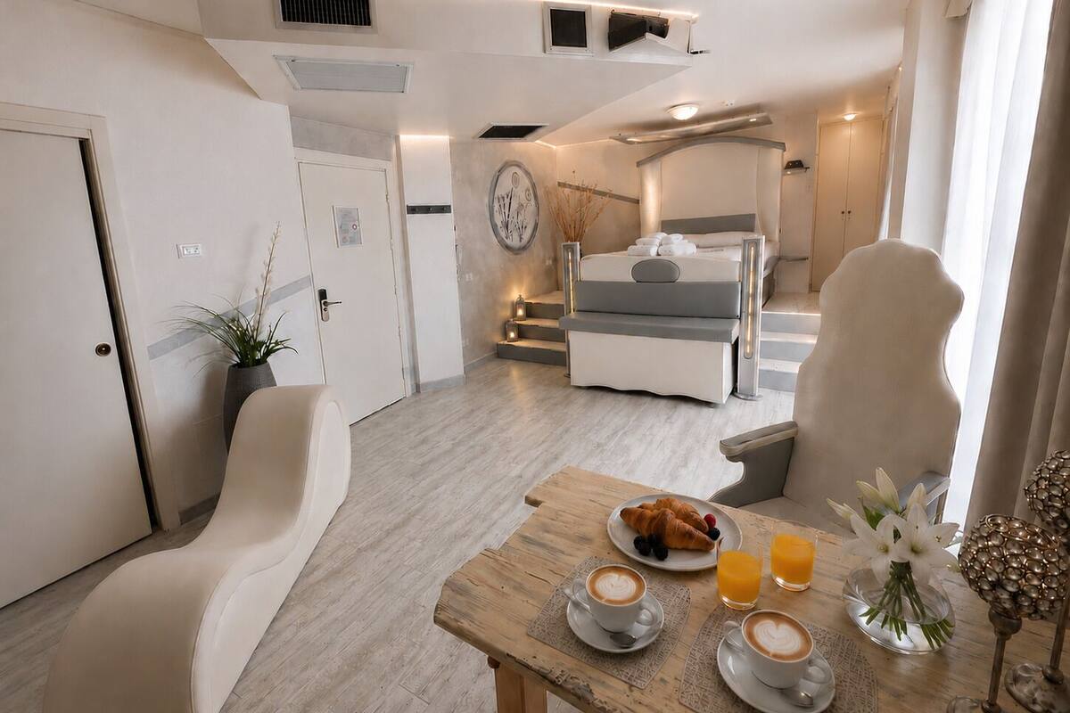 Una camera d'albergo moderna con un letto, un tavolo da pranzo con colazione, e una scala che conduce a un piano superiore.