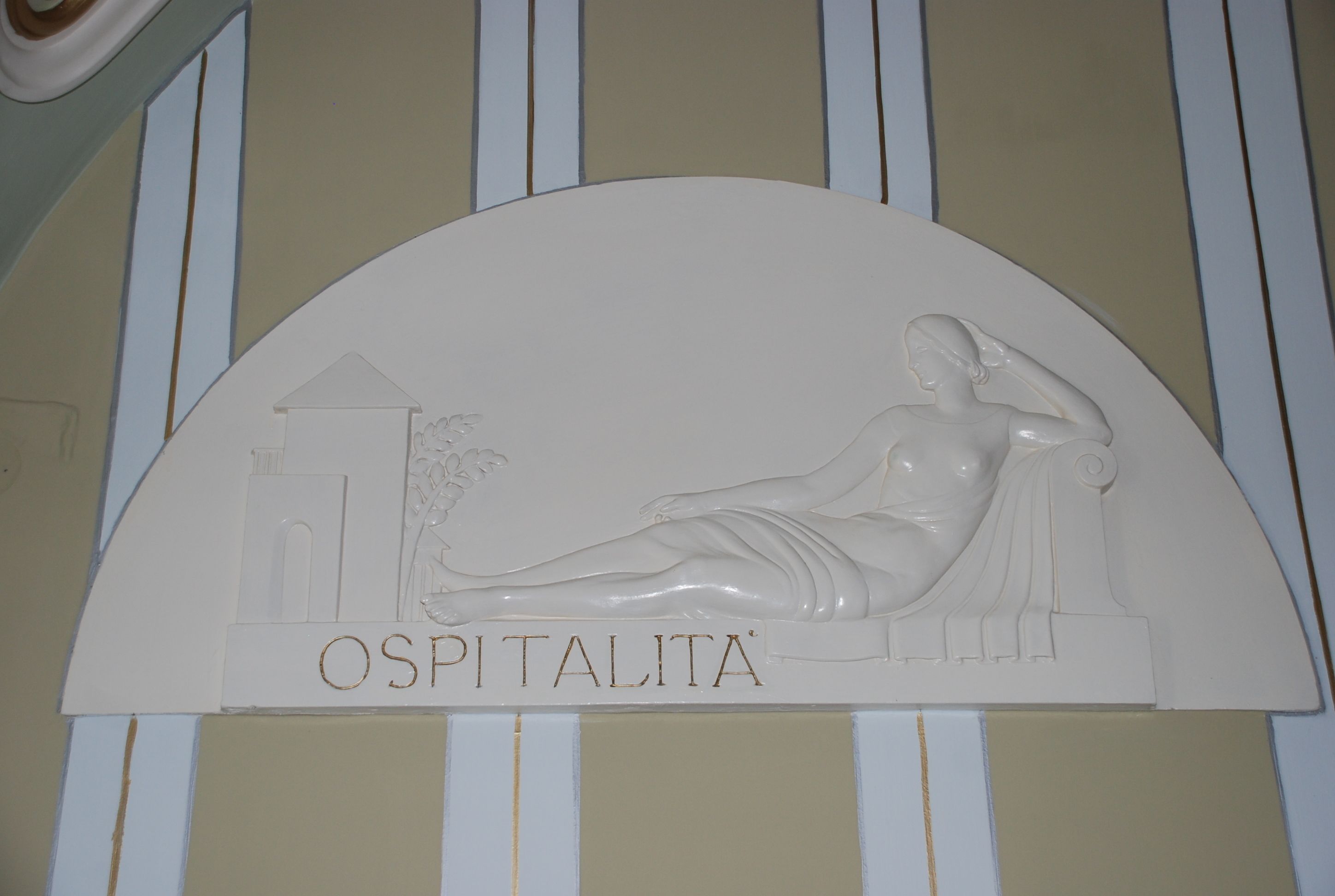 A white relief sculpture with the name "OSPITALITA" on a wall.