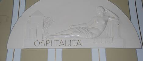 A white relief sculpture with the name "OSPITALITA" on a wall.