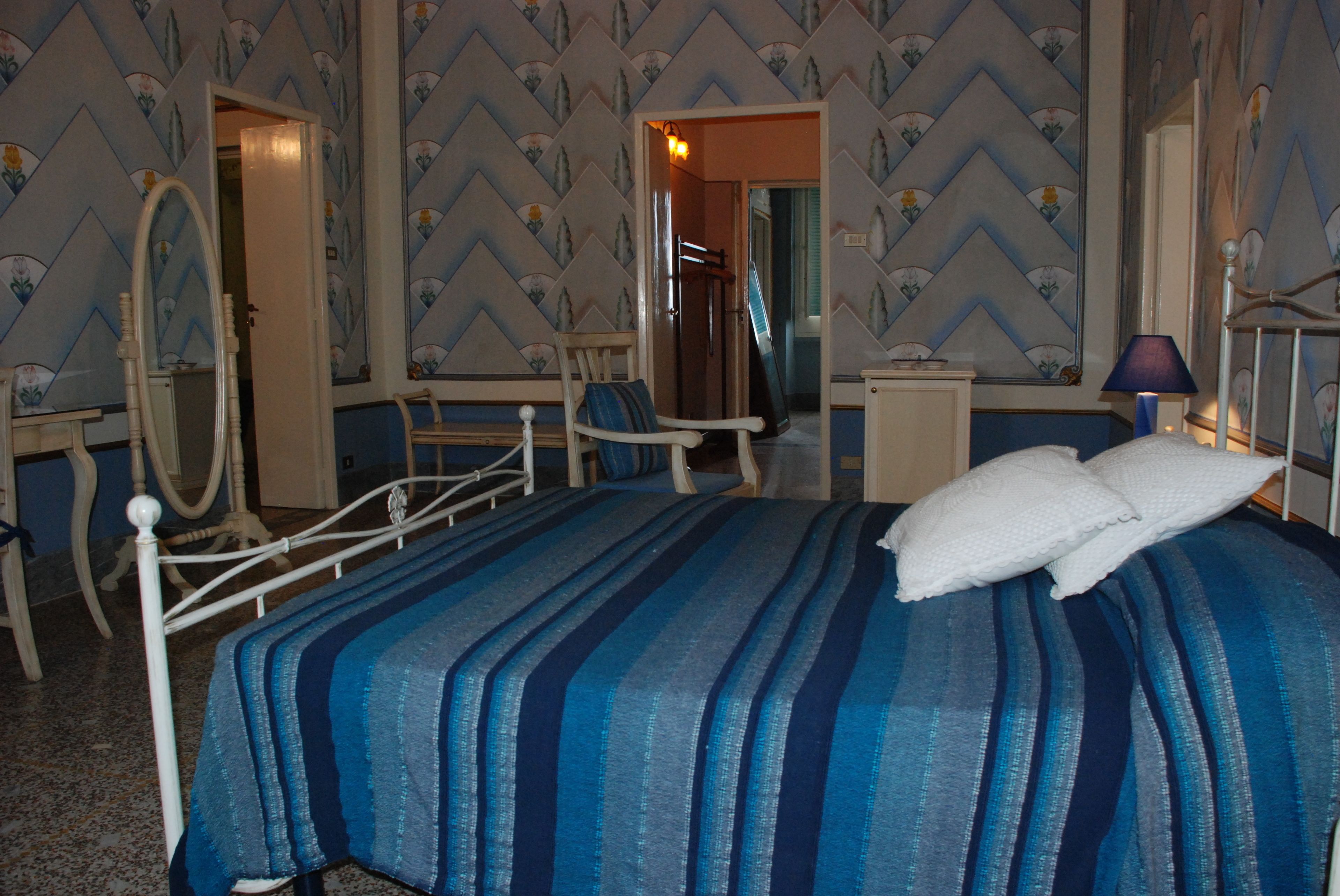 Habitación de hotel con cama, una silla, escritorio, espejo y puerta que da a otra habitación.