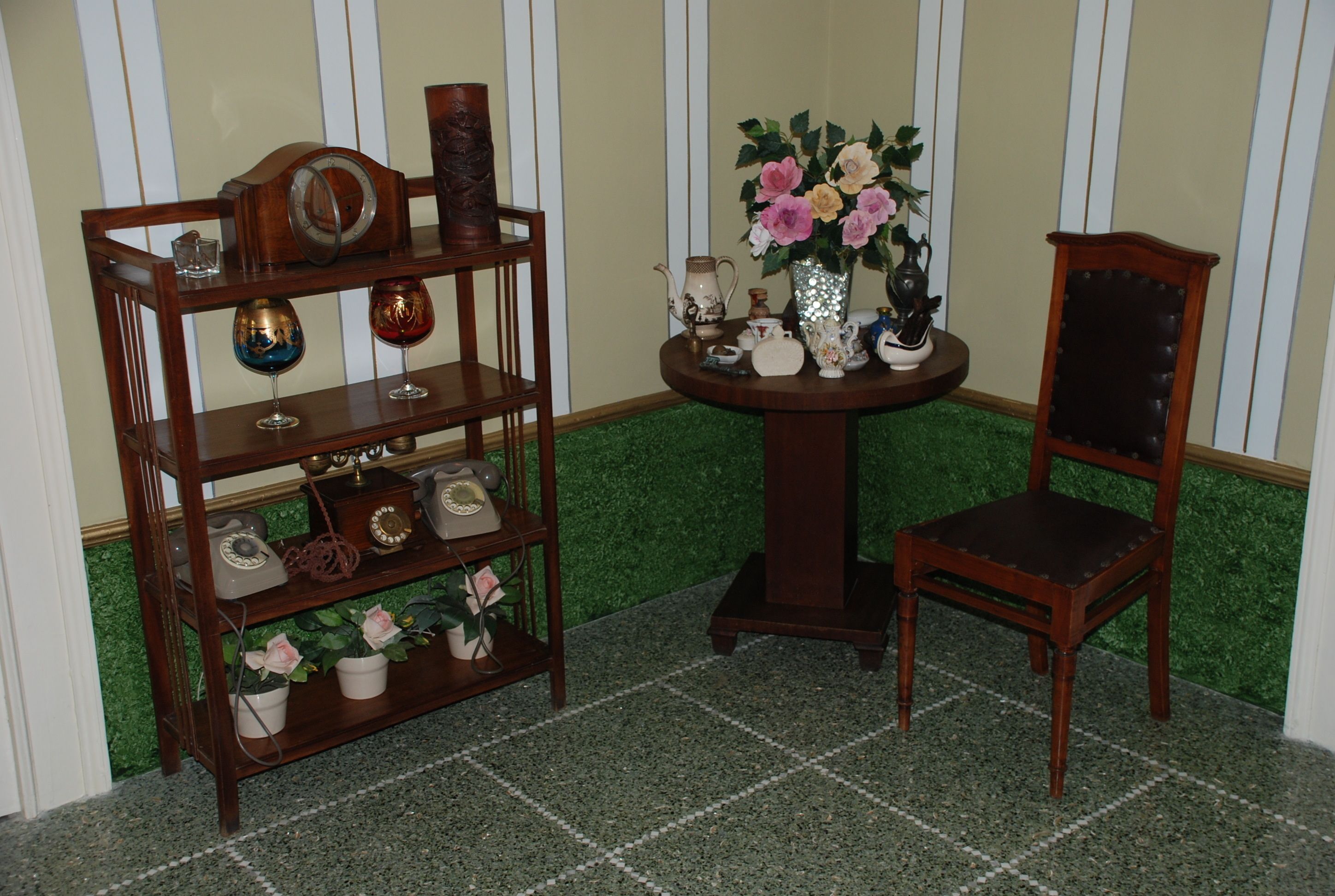 Una silla de madera y una estantería con varios objetos, entre ellos un jarrón de flores, un teléfono y adornos.