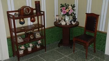 Una silla de madera y una estantería con varios objetos, entre ellos un jarrón de flores, un teléfono y adornos.