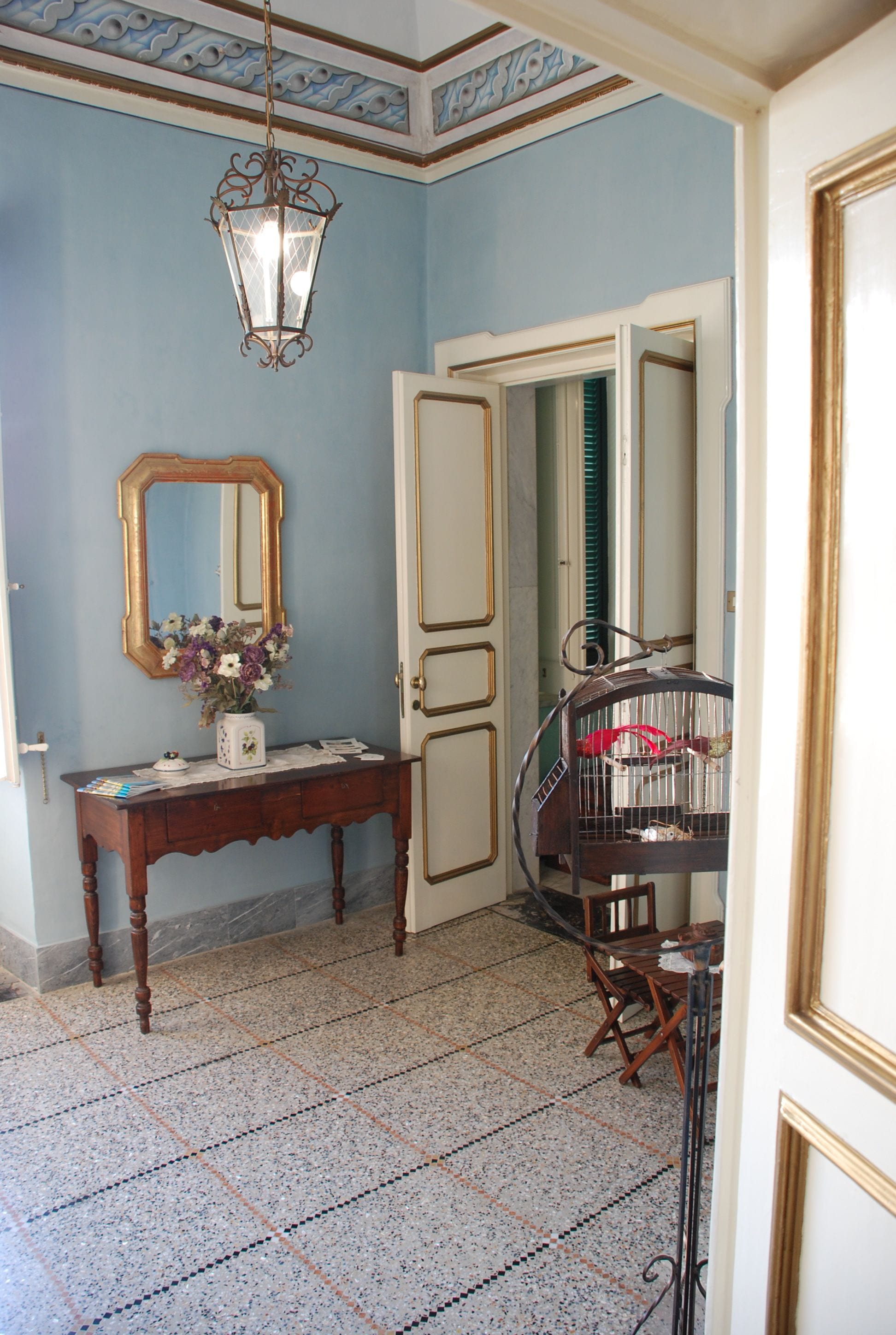 A room with a wooden console table, a mirror, a birdcage, and a tiled floor.