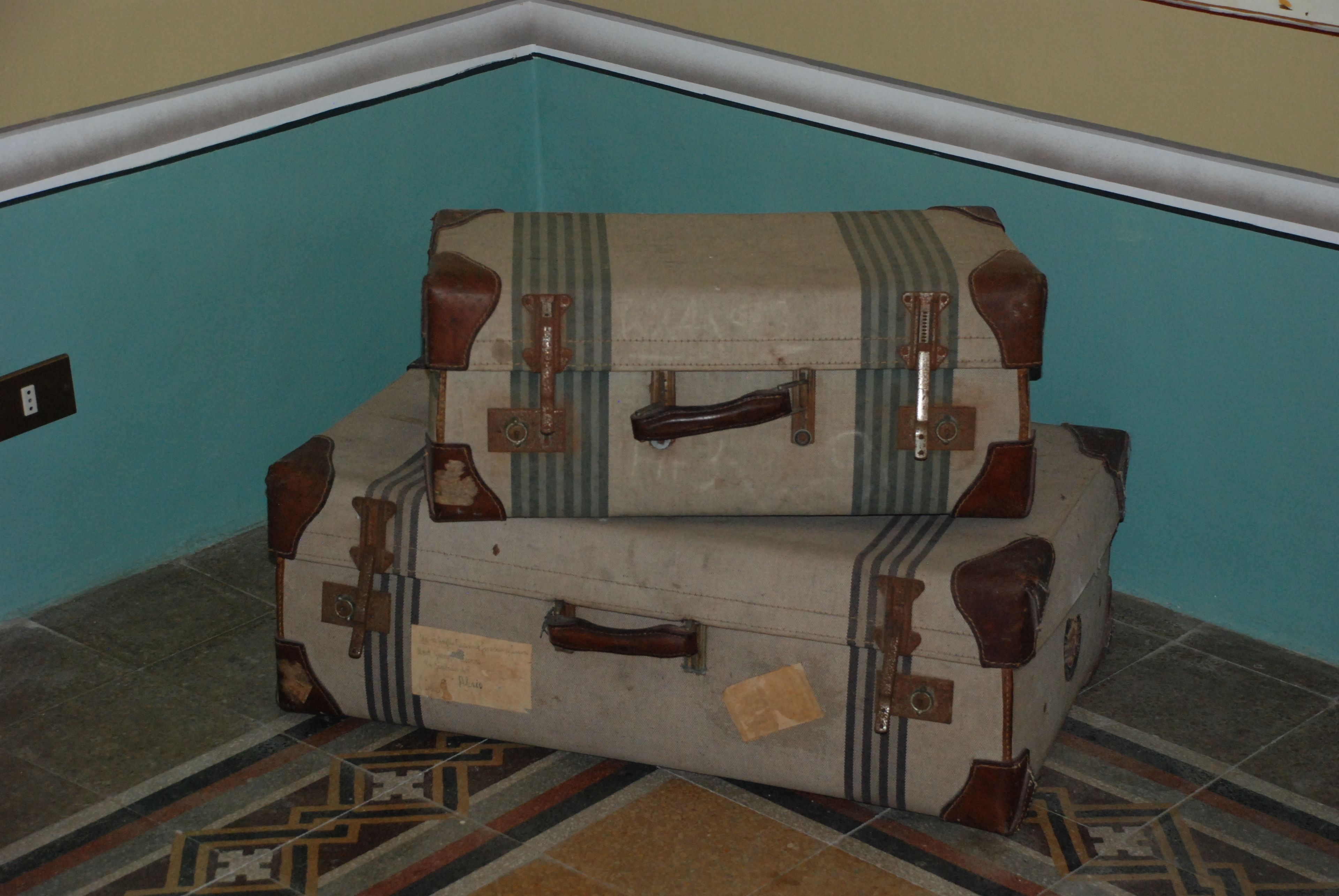 Two stacked suitcases with leather straps and metal clasps, placed on a patterned floor.