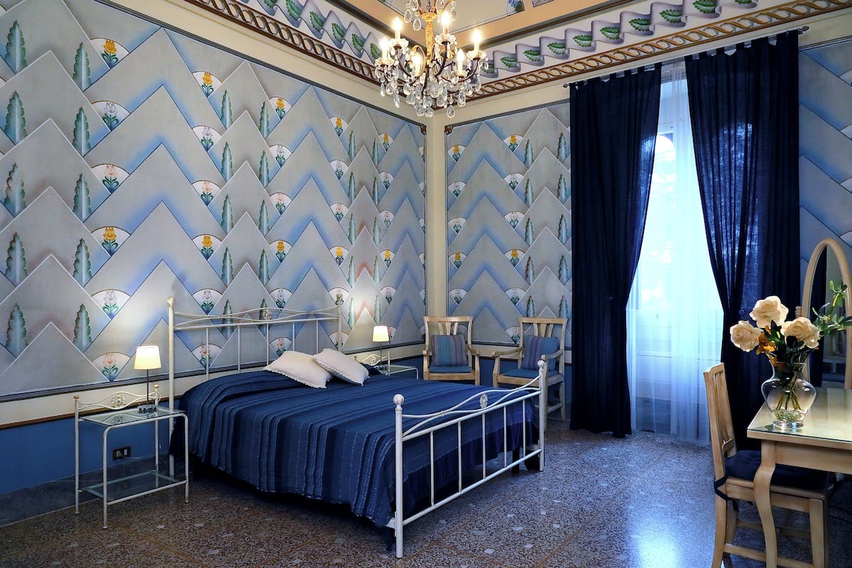 A bedroom with a bed, bedside tables, a chair, a desk, and a chandelier.
