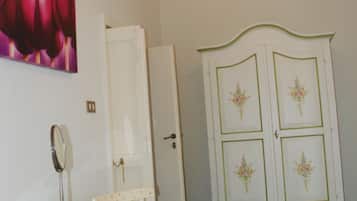 Une pièce avec une table ronde en verre, une chaise blanche, un meuble blanc orné de motifs floraux et un tableau représentant des fleurs accroché au mur.
