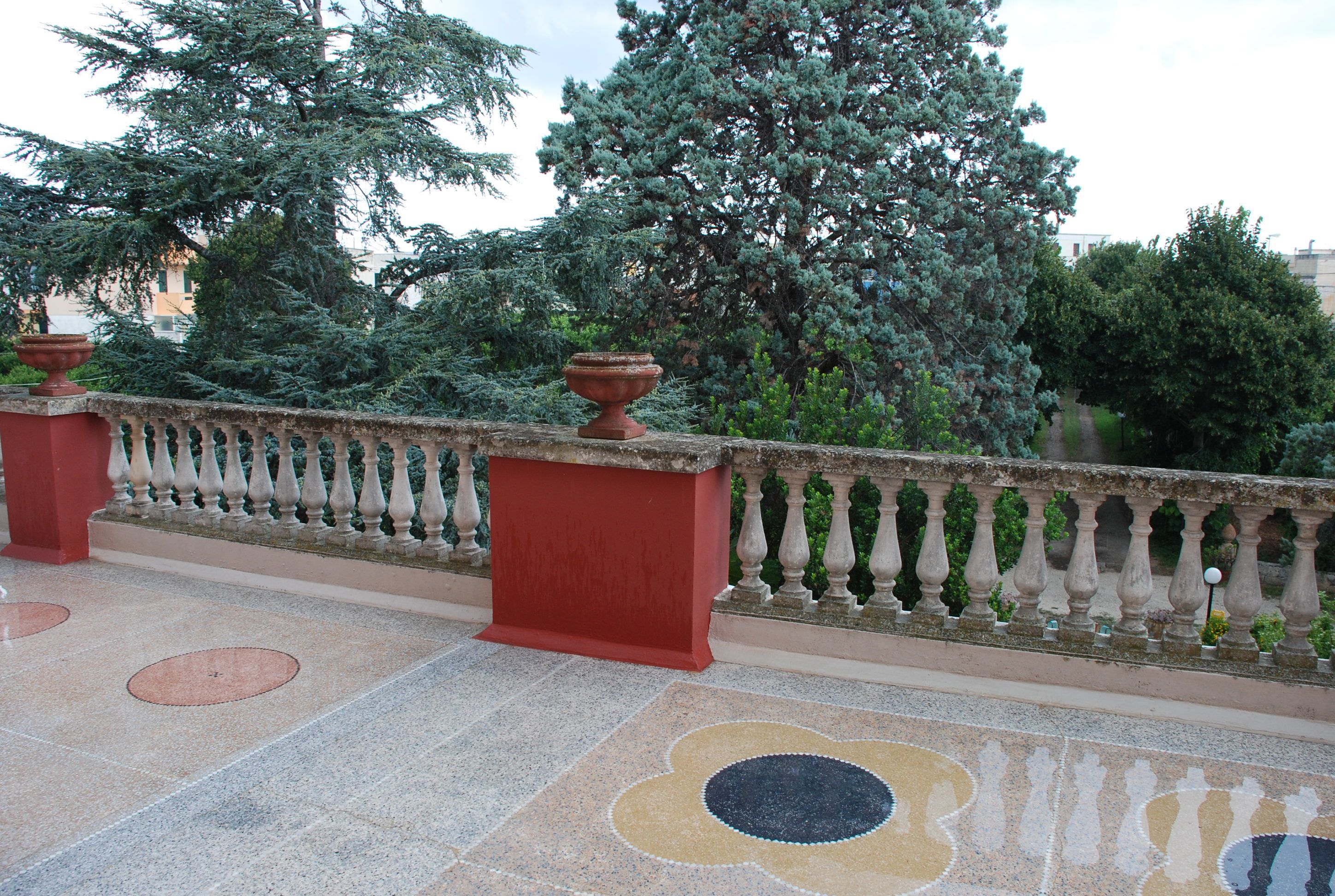 A terrace with a patterned floor, a red column, and a balustrade.