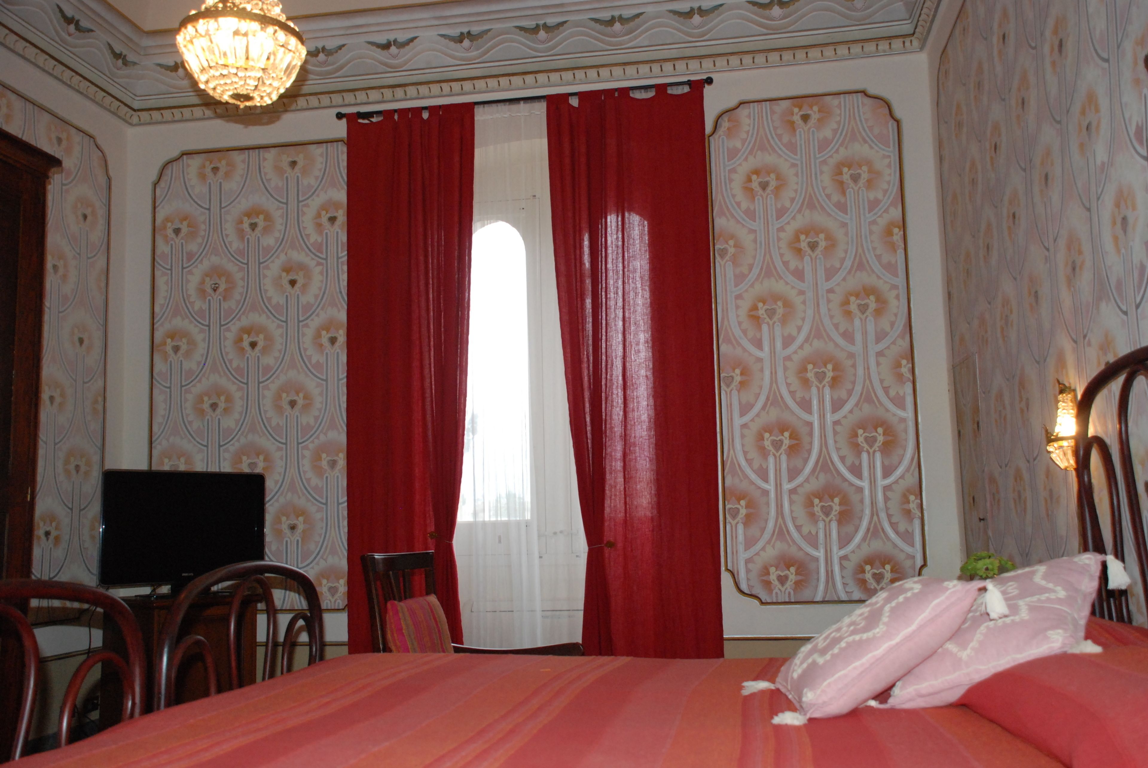 A bedroom with a bed, a television, and a window with red curtains.