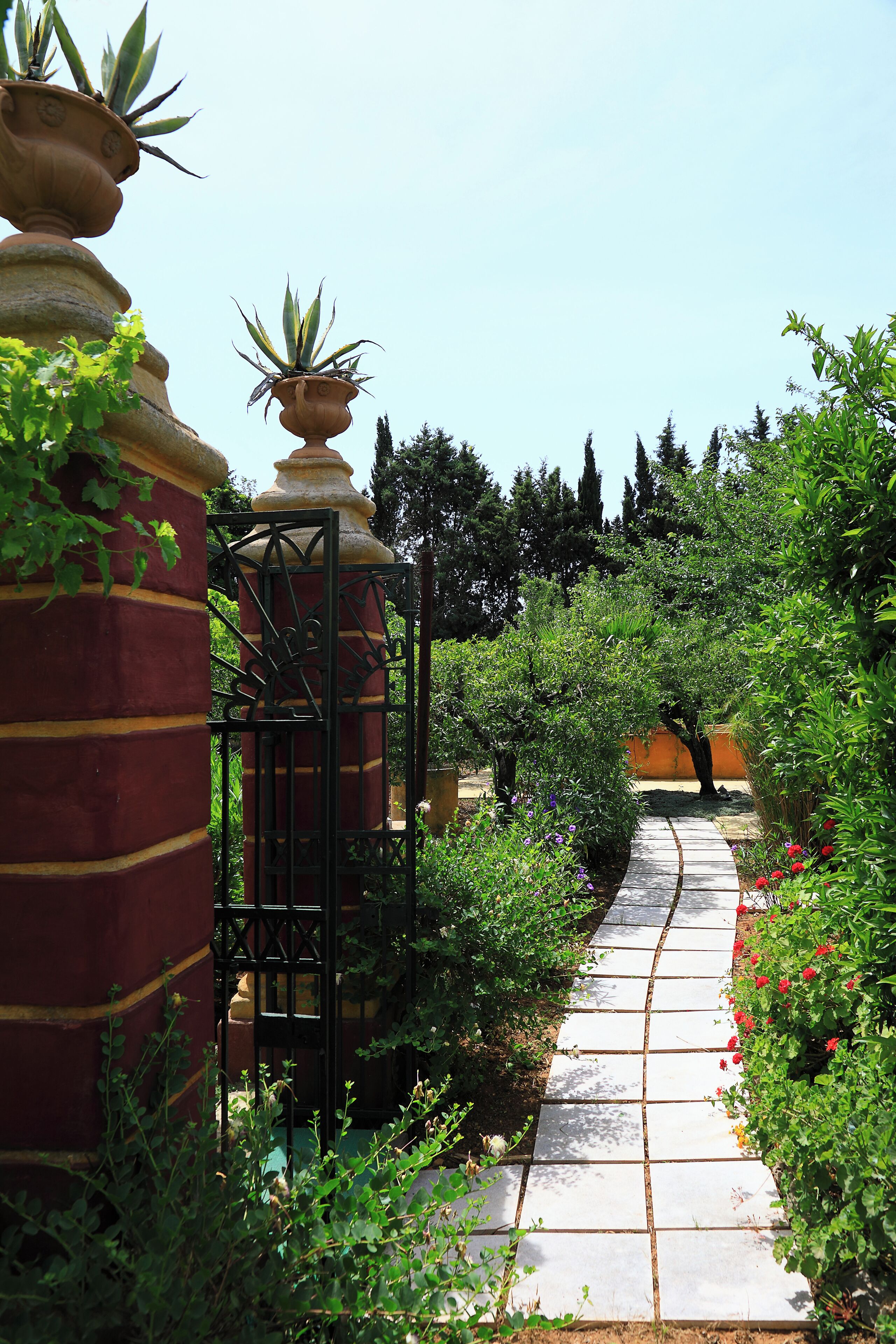 Un sendero de jardín con suelo de piedra, rodeado de abundante follaje y flores rojas.