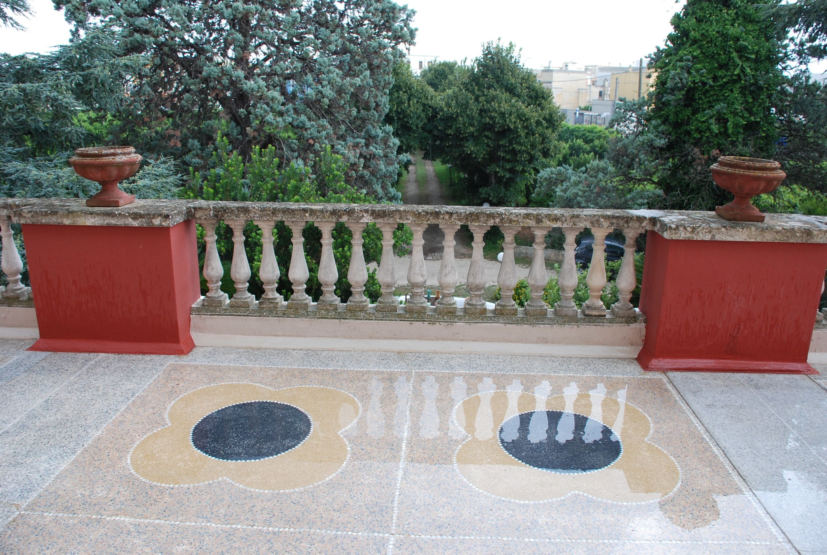 A balcony with a tiled floor featuring a floral pattern, a balustrade, and two terracotta pots.