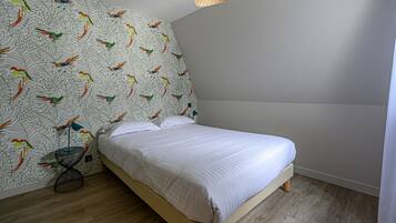 A bedroom with a bed, a wall with a bird pattern, a small table with a lamp, and a hanging light fixture.