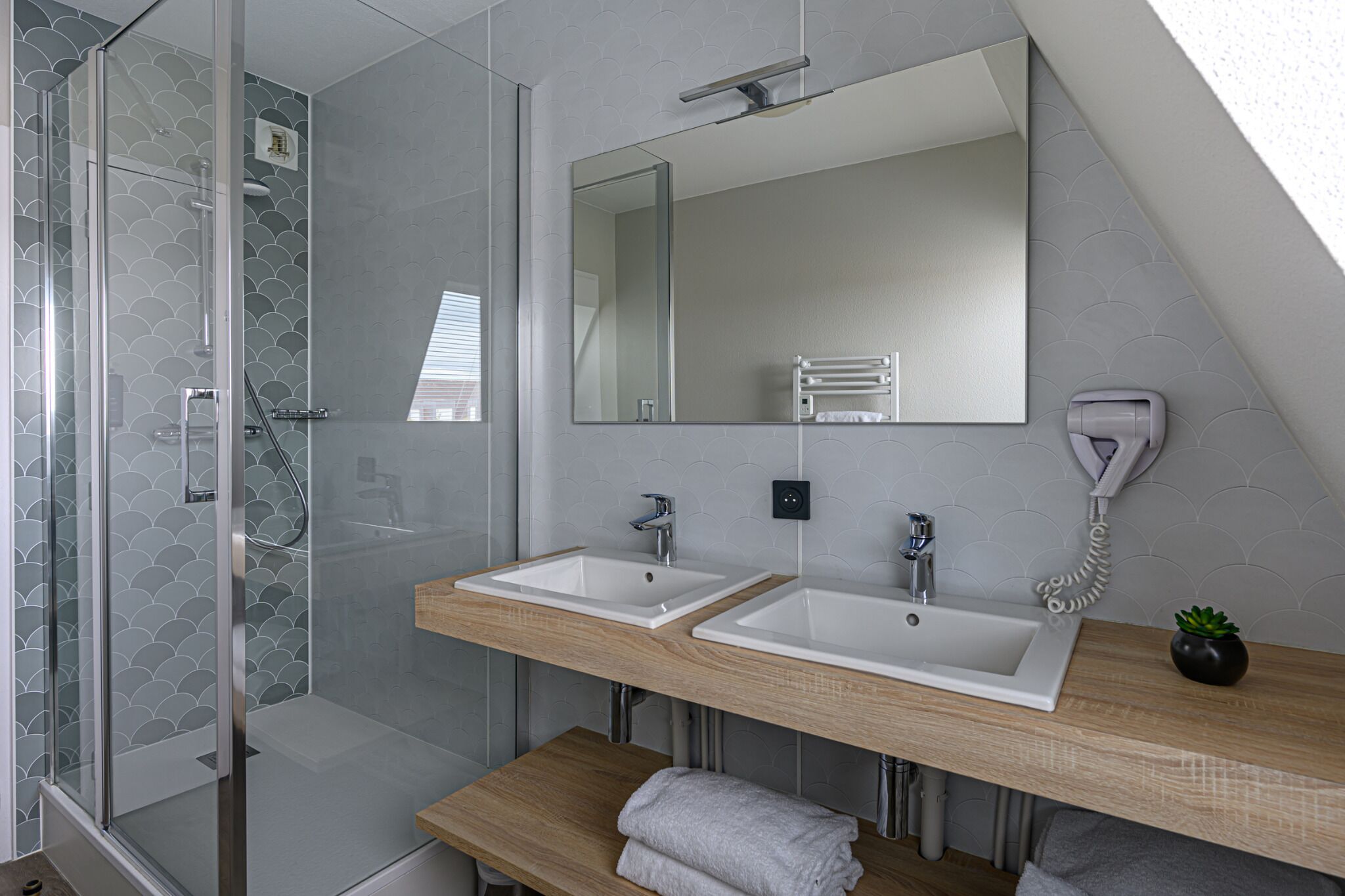 Een moderne badkamer met twee wasbakken, een douche en een grote spiegel.