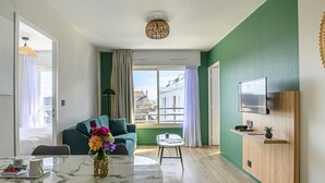 Una sala moderna con una pared verde decorativa, un comedor con una mesa de mármol y una cocina con mostrador de madera y televisor.