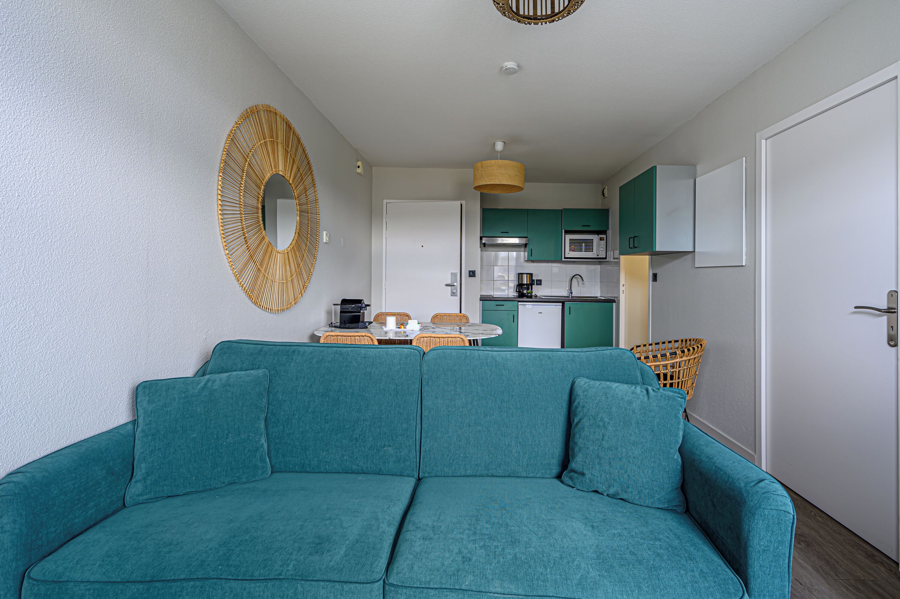 A teal sofa in a living area with a kitchen in the background.