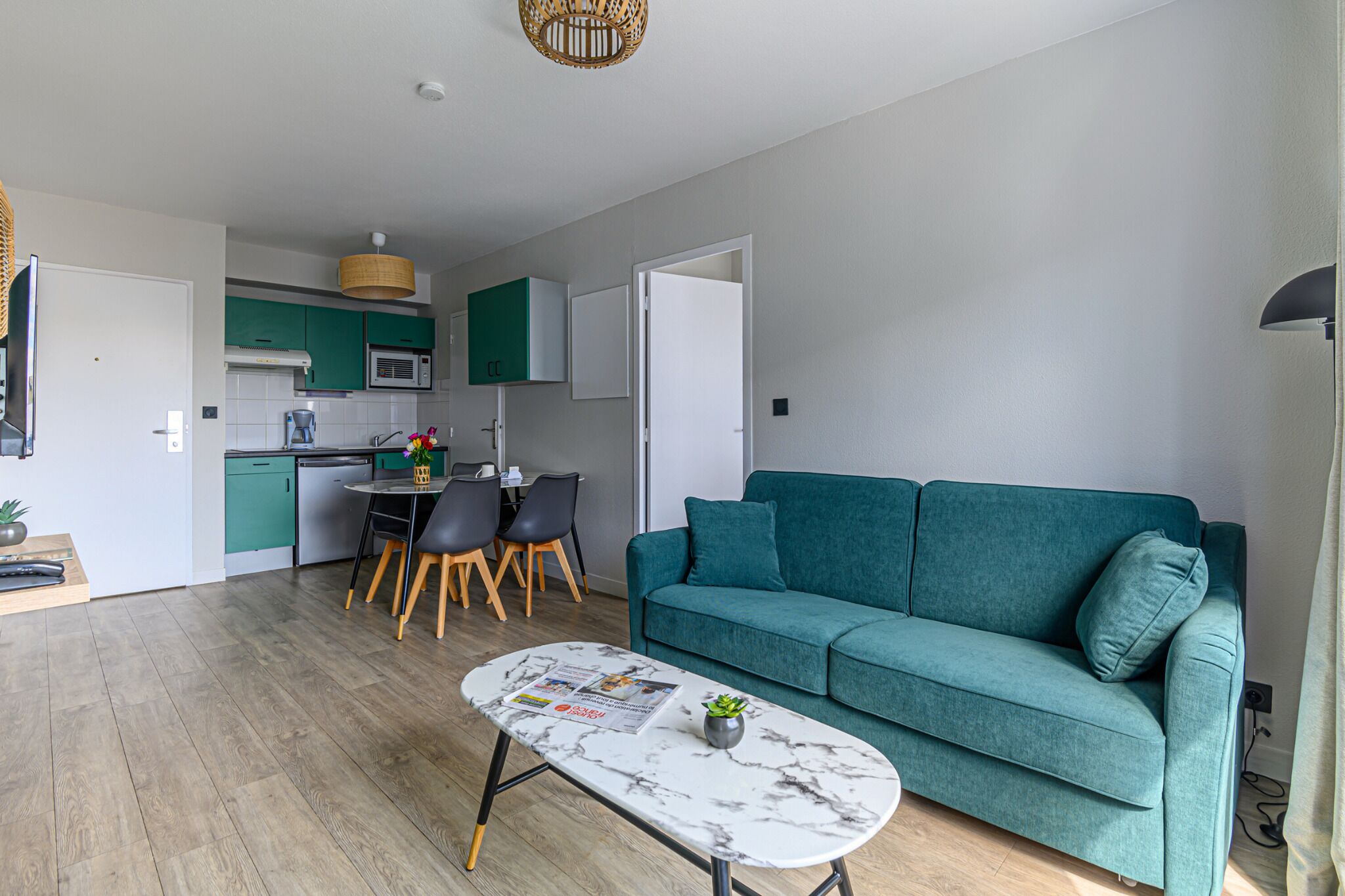 A modern living room with a teal sofa, a marble coffee table, and a dining area with a small table and chairs.