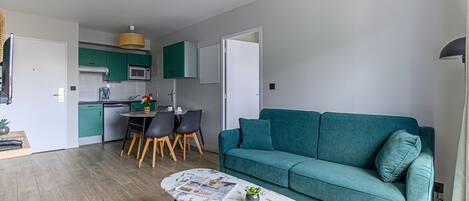 A modern living room with a teal sofa, a marble coffee table, and a dining area with a small table and chairs.