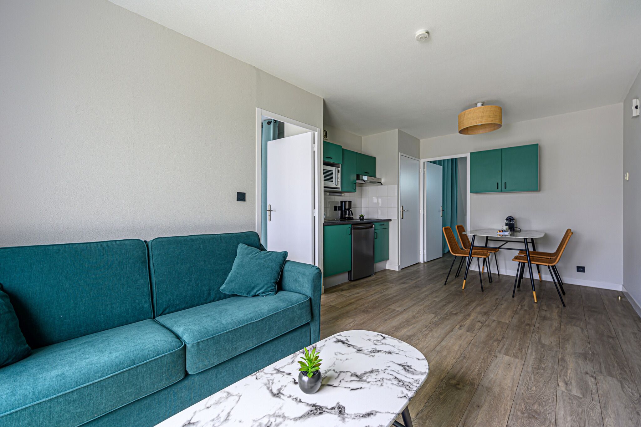 Ett modernt vardagsrum med en turkos soffa, ett soffbord i marmor och en matplats med trästolar och ett bord.