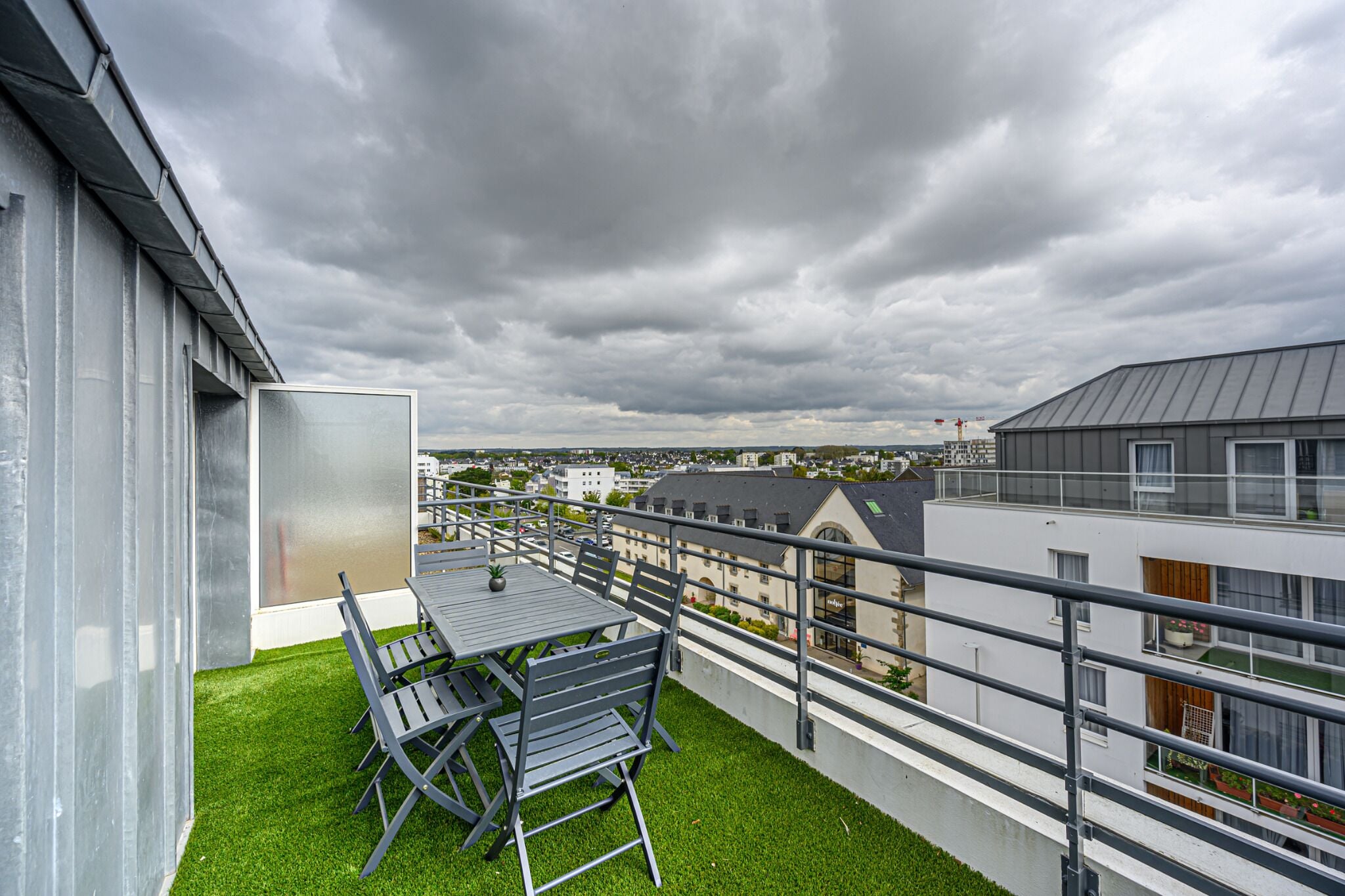 Un balcon avec une table et des chaises, une vue sur la ville et un ciel nuageux.