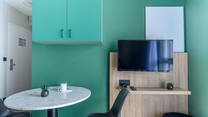 Una habitación moderna con una pared verde, una pizarra, un televisor de pantalla plana, una mesa redonda con dos sillas y una planta pequeña.
