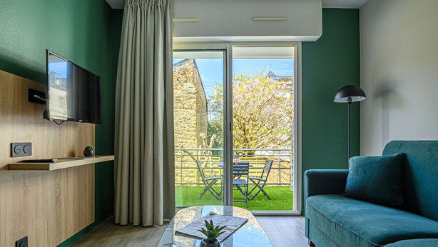 Una sala de estar moderna con un sofá verde, un televisor de pantalla plana, un estante de madera y una mesa de vidrio con una planta.