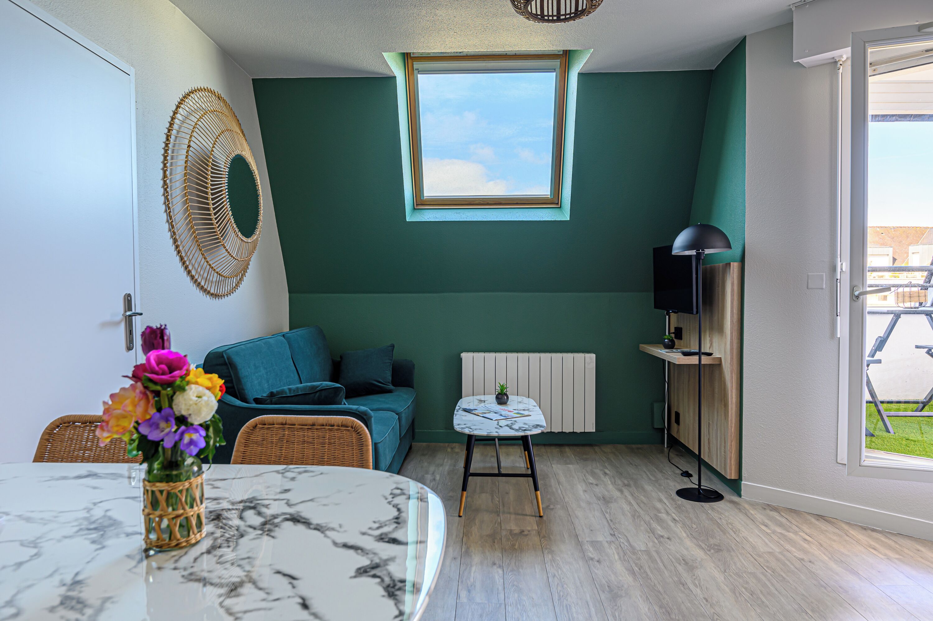 Une pièce avec un mur de couleur turquoise, une fenêtre, un canapé, une petite table, une lampe et une vue sur l’extérieur.