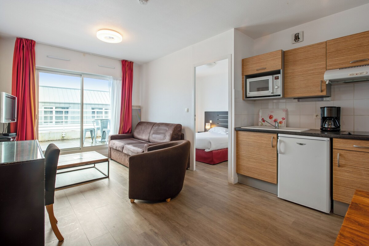Et moderne hotelværelse med balkon, tekøkken, spiseplads og seng.