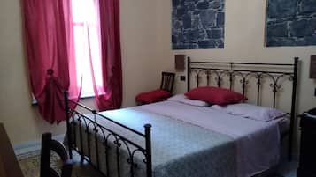 Une chambre à coucher avec un lit, une chaise, une fenêtre avec des rideaux rouges et un mur en pierre.